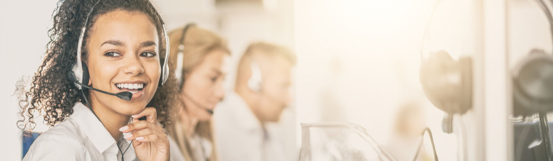 young lady with headset on customer service call with colleagues in back ground