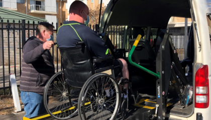 man wheeling wheelchair passenger into WAT wearing mask
